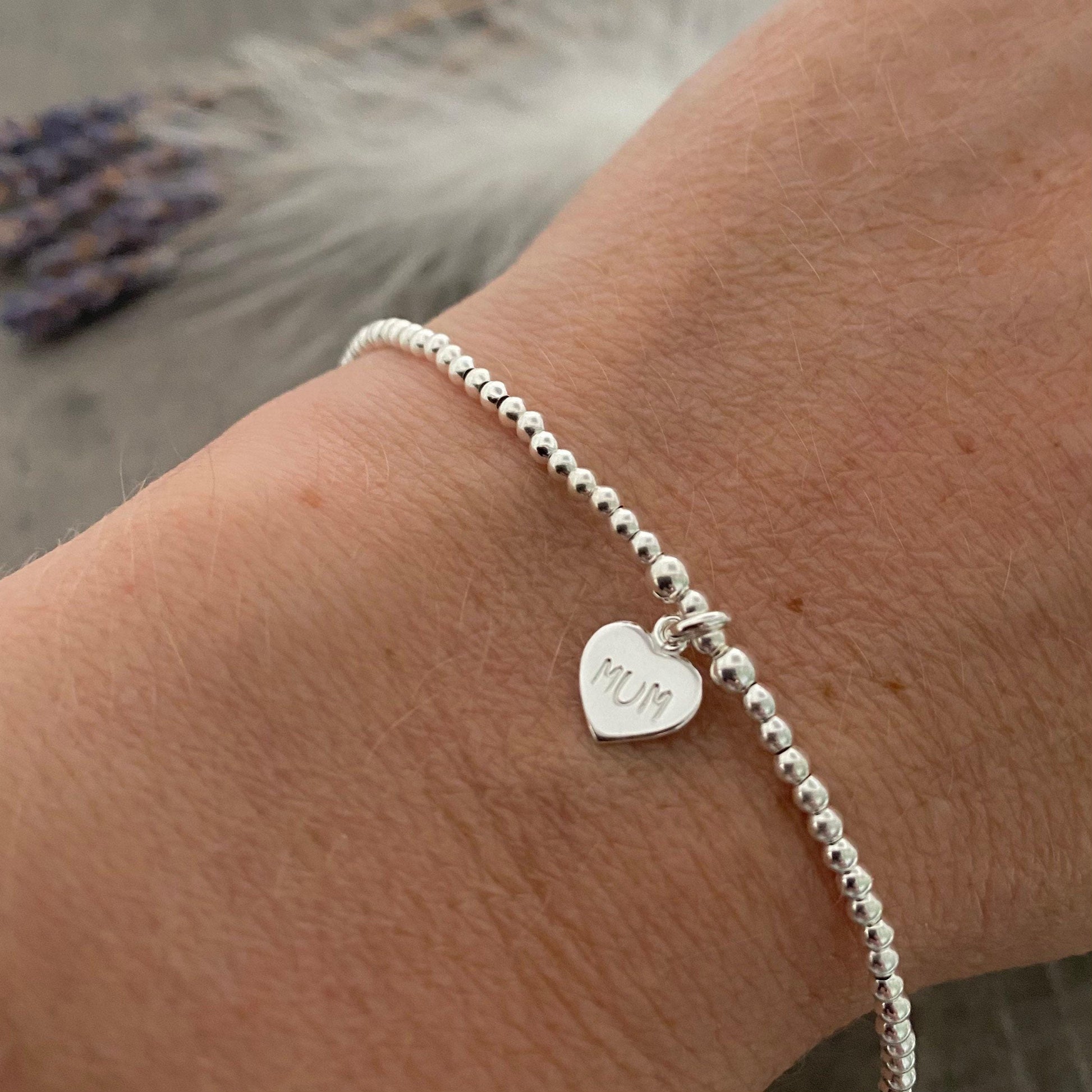 A thin sterling silver beaded bracelet with mum stamped in a silver heart charm on the bracelet